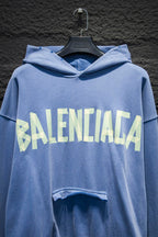 Light blue hoodie with hood and large front graphic text; front pocket opening detail visible