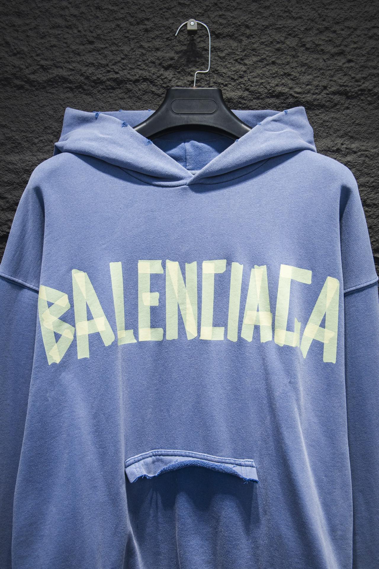 Light blue hoodie with hood and large front graphic text; front pocket opening detail visible