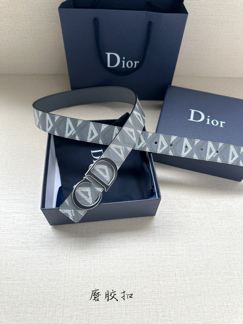 Designer belt laid on blue box with gray monogram strap and silver-tone double buckle