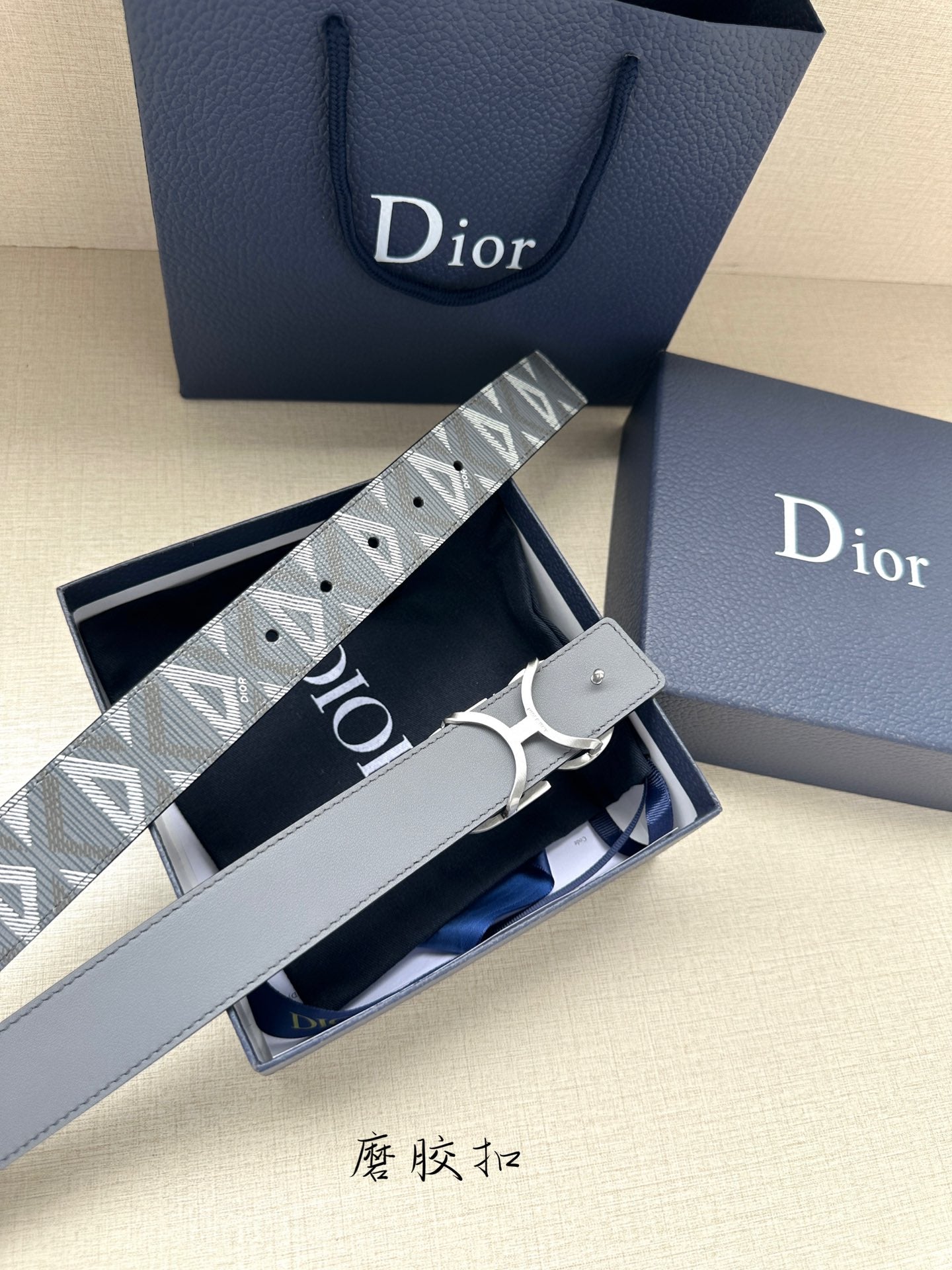 Designer belt with gray monogram strap and silver-tone buckle shown in packaging