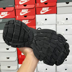 Black sneaker outsole with deep tread pattern, underside view