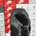 Black athletic sneaker with mesh collar and lace-up front, close-up heel view
