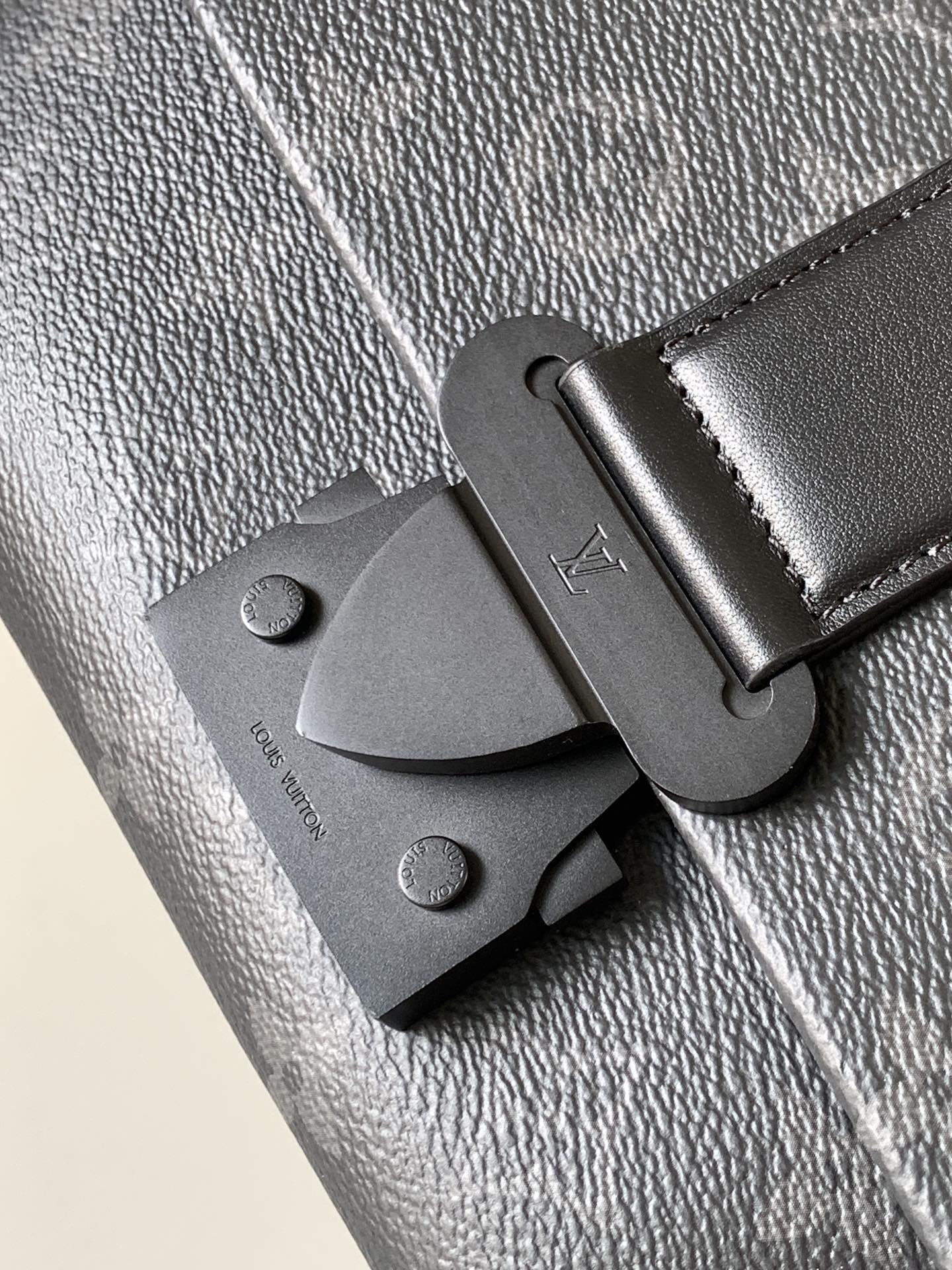 Louis Vuitton bag clasp and strap tab, dark leather, textured finish, metal hardware.