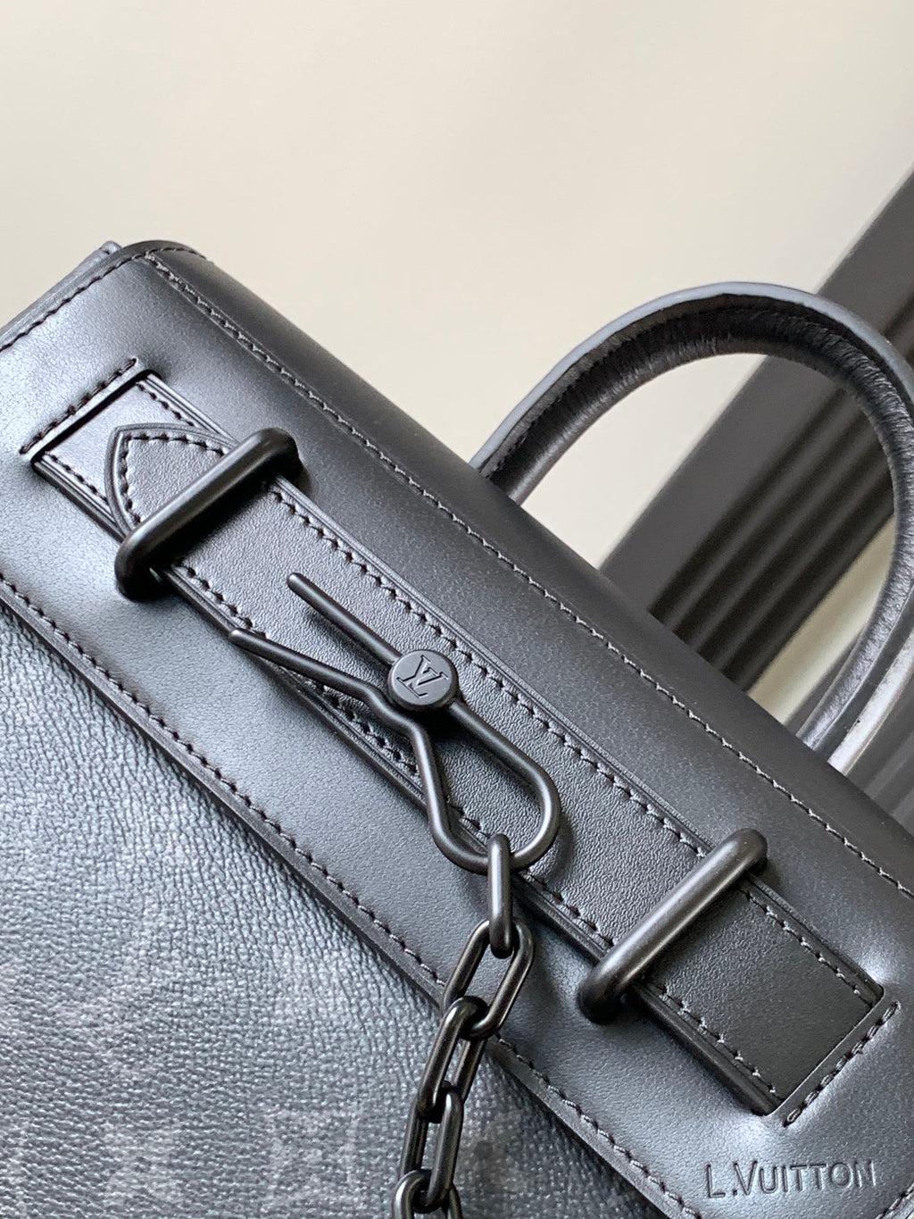 Louis Vuitton monogram handbag close-up with front hardware and stitched strap, dark gray.