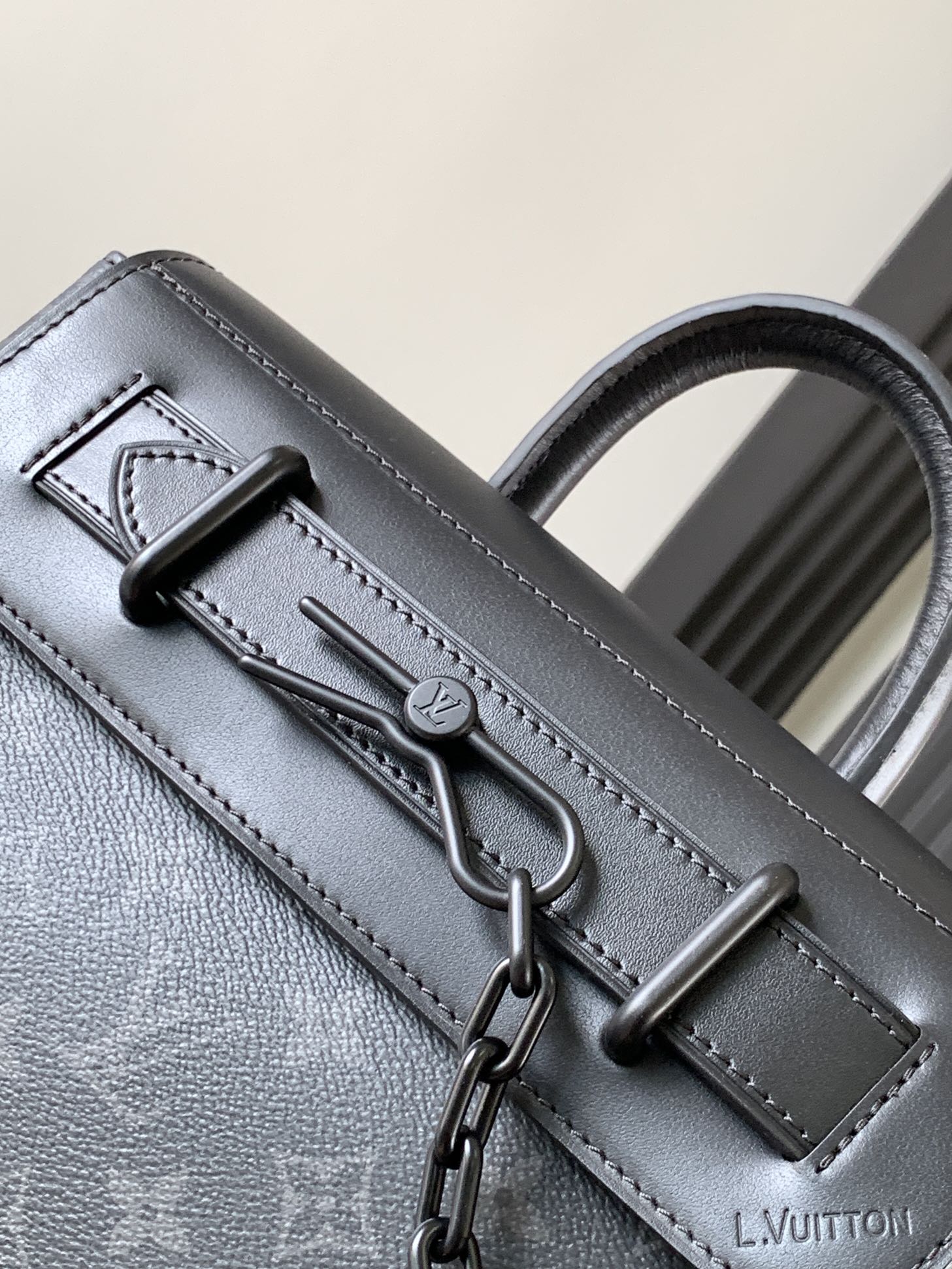 Louis Vuitton monogram handbag close-up with front hardware and stitched strap, dark gray.