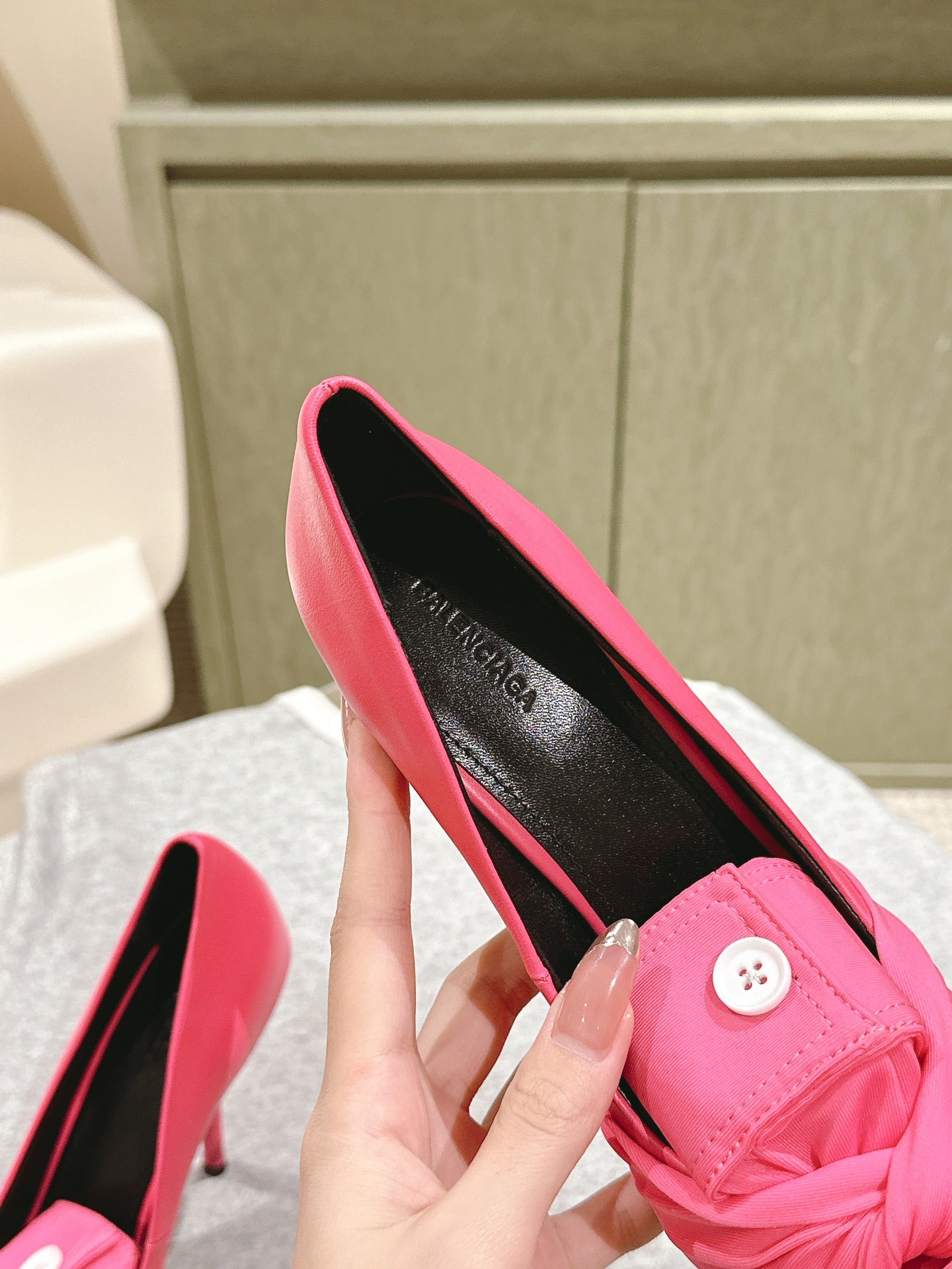 Pink stiletto sandals held by heel, showing black insole and knotted front strap