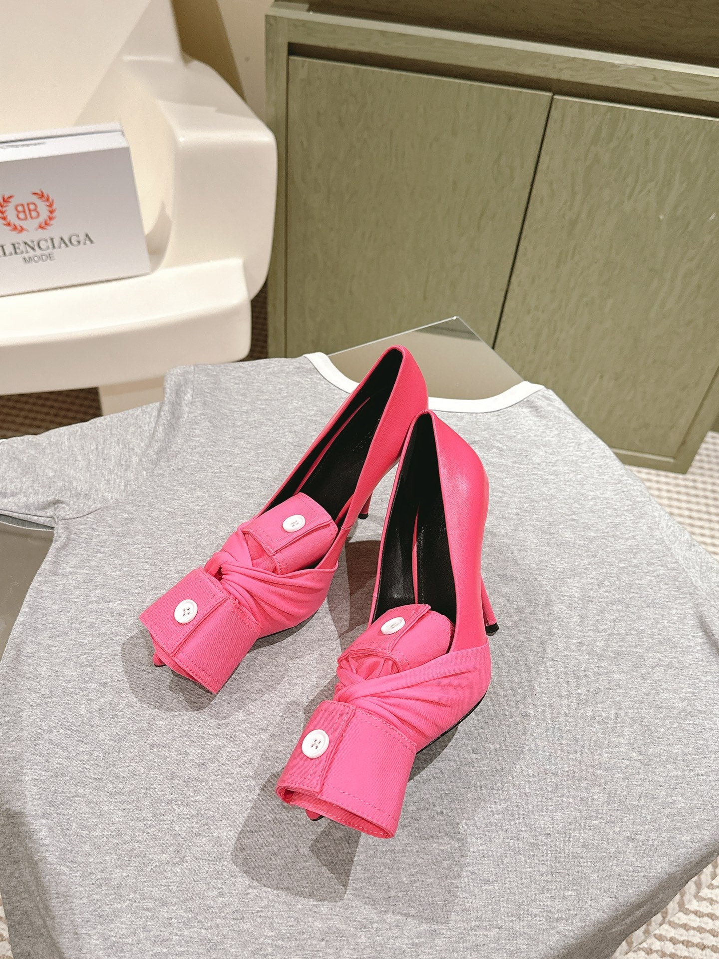Pink sandals with twisted front straps, white button accents, black interior, stiletto heel