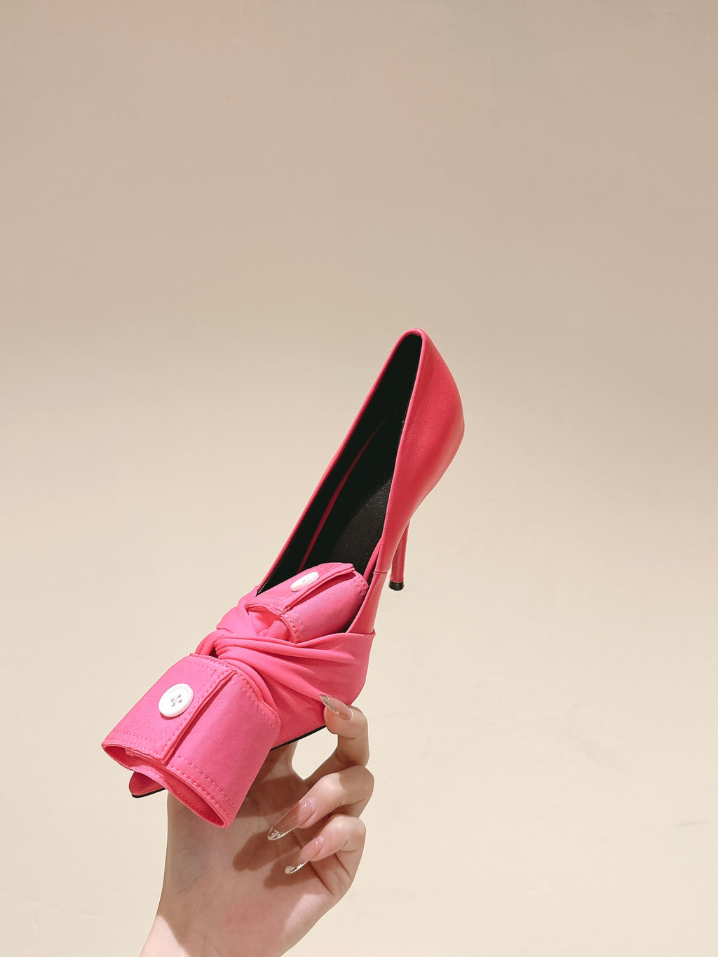 Pink heeled sandals held in hand, featuring knotted front strap and black insole