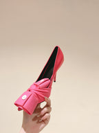 Pink heeled sandals held in hand, featuring knotted front strap and black insole