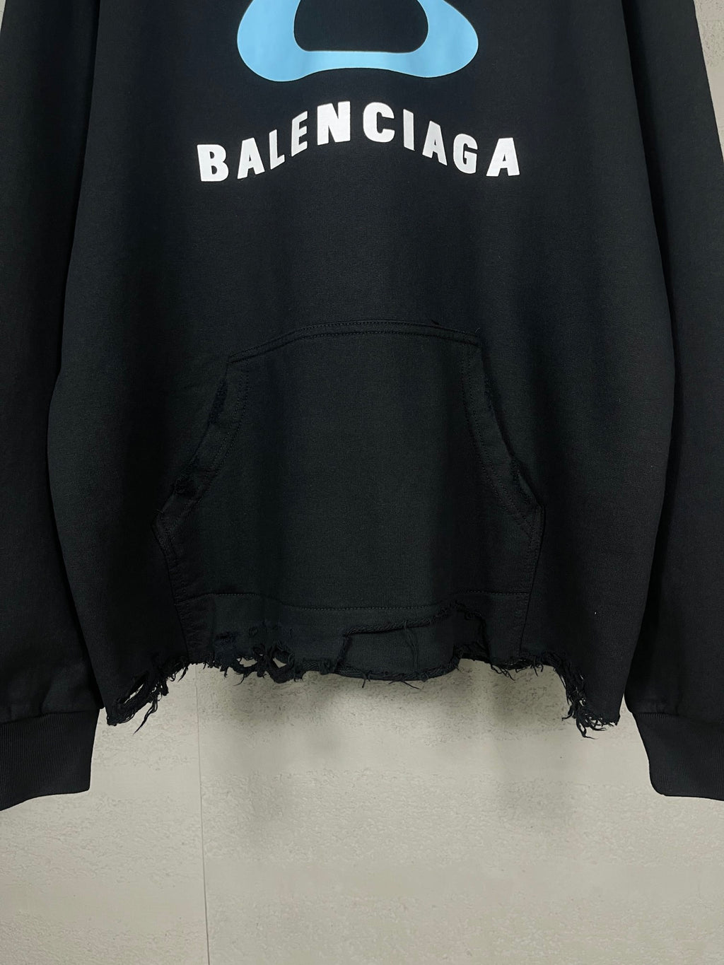 Black long hoodie with blue logo, kangaroo pocket, and frayed bottom edge