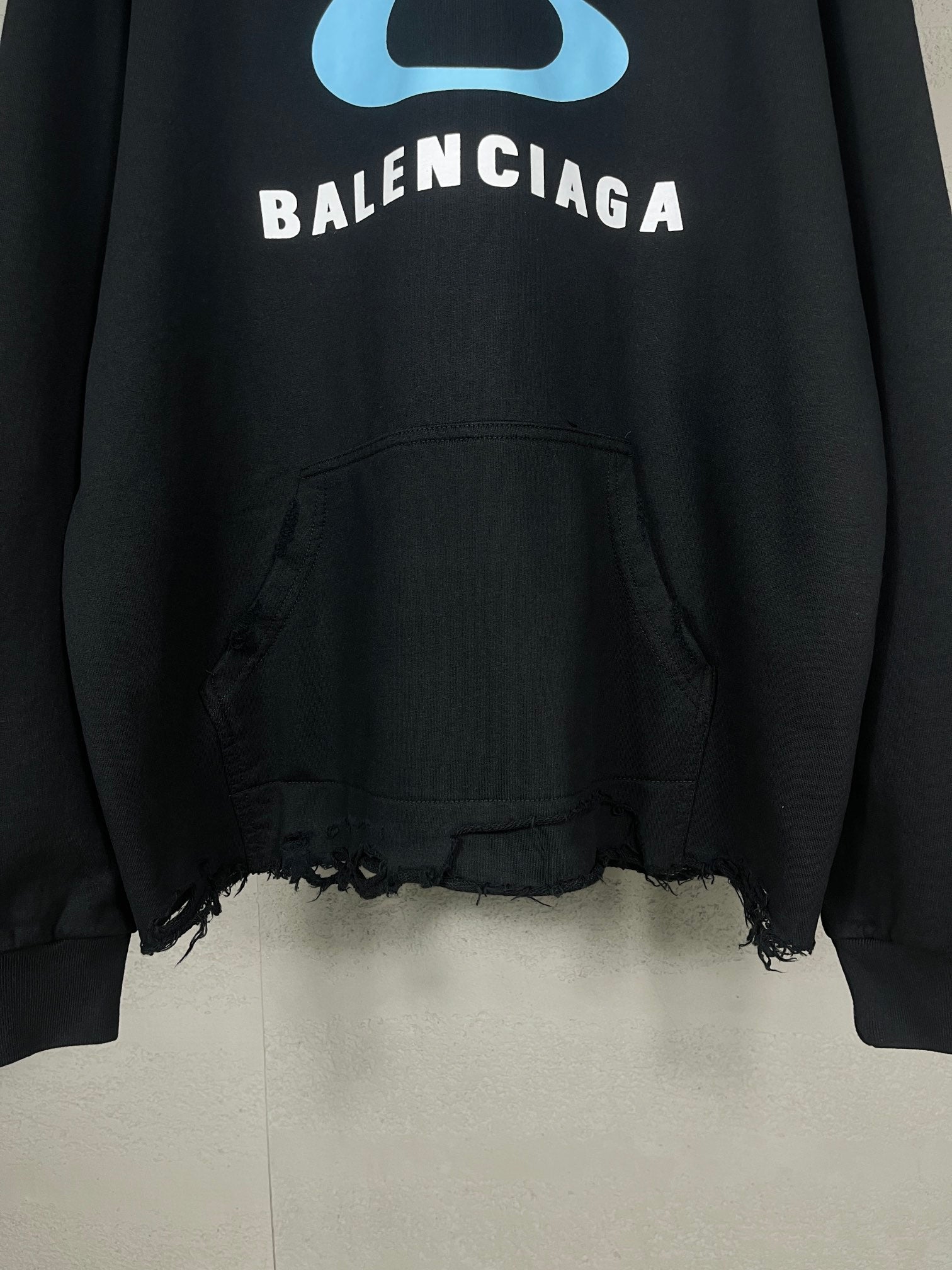 Black long hoodie with blue logo, kangaroo pocket, and frayed bottom edge