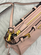 Pink leather shoulder bag with front straps, gold-tone hardware, and zipper pulls
