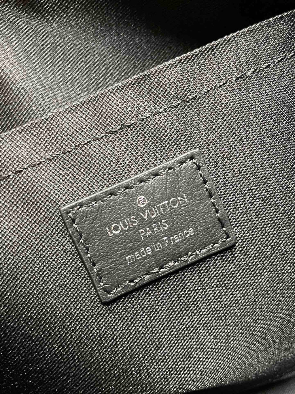 Leather brand label reading Louis Vuitton on monogram canvas bag