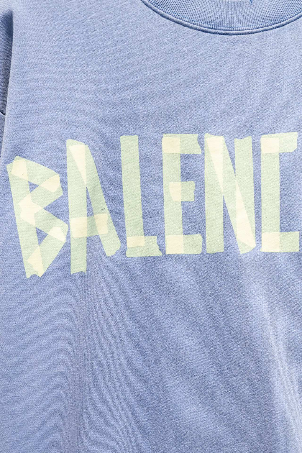 Light blue sweatshirt close-up of Balenciaga wordmark print in pale yellow.
