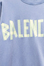 Light blue sweatshirt close-up of Balenciaga wordmark print in pale yellow.