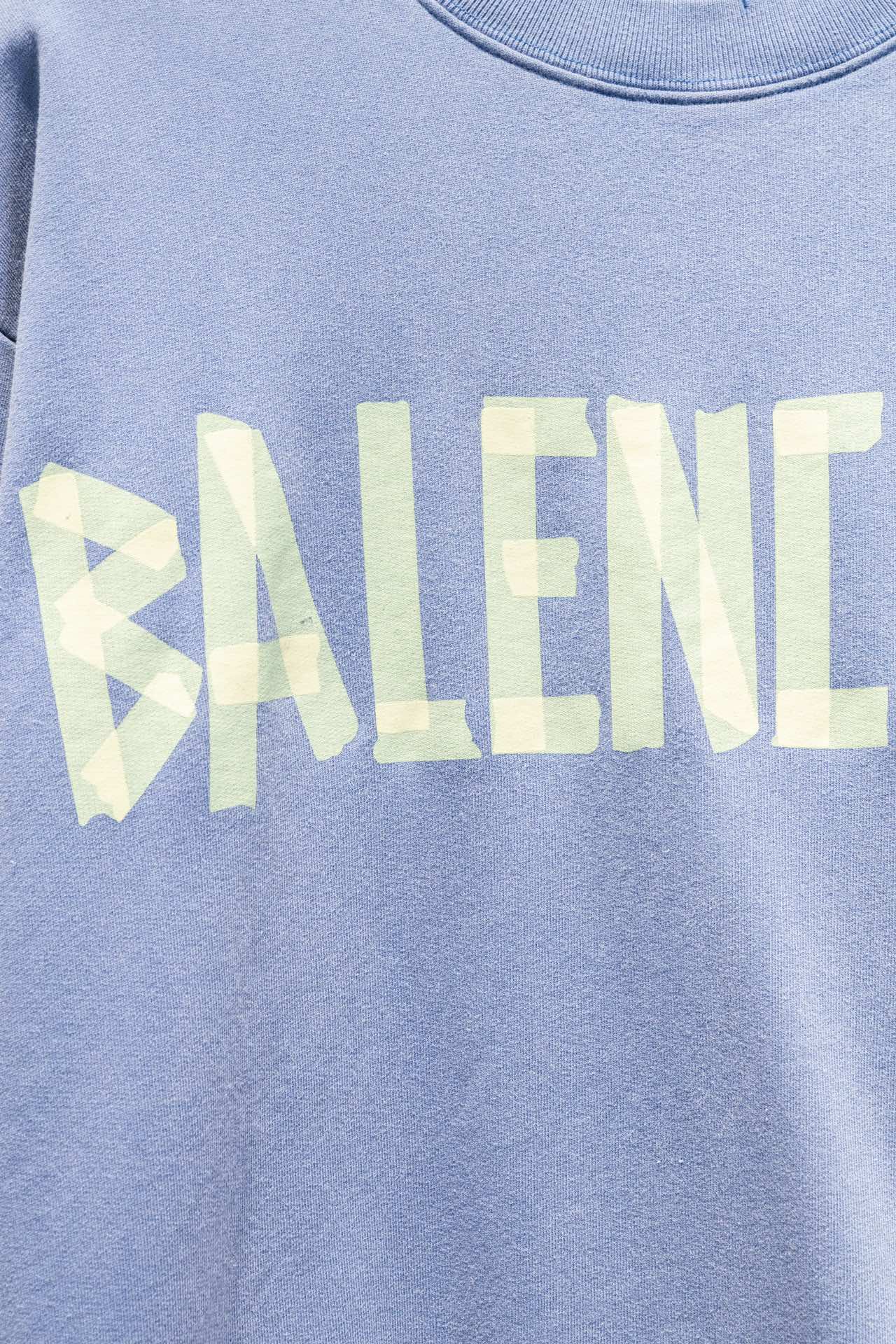 Light blue sweatshirt close-up of Balenciaga wordmark print in pale yellow.