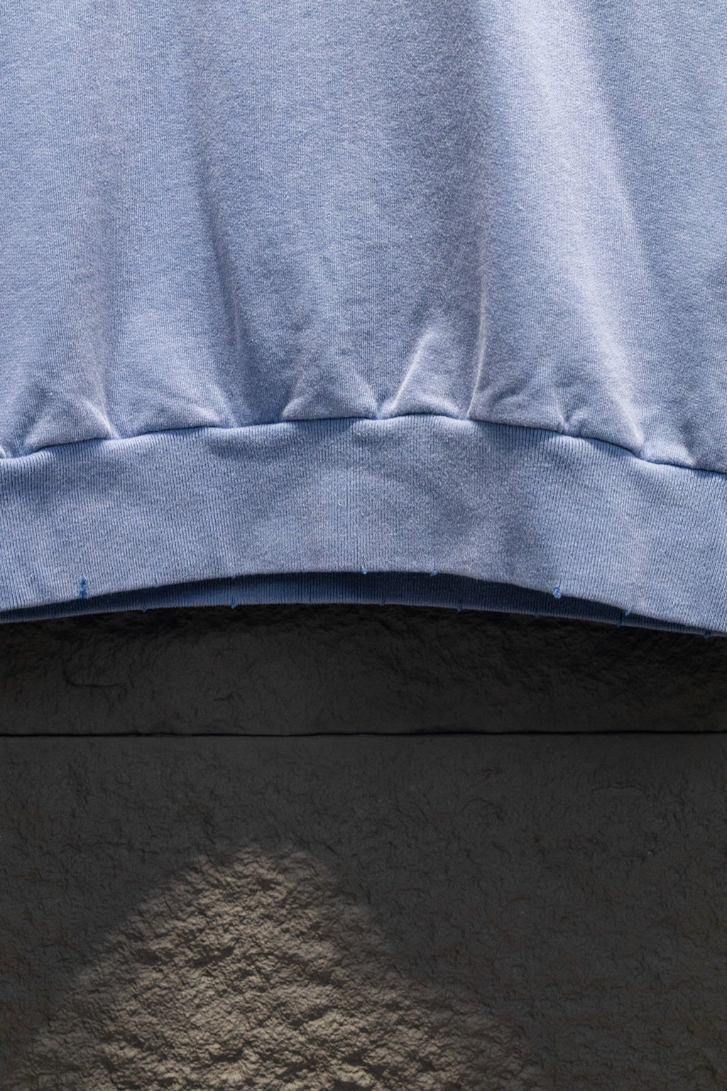 Light blue sweatshirt hem with ribbed band and stitched seam detail.