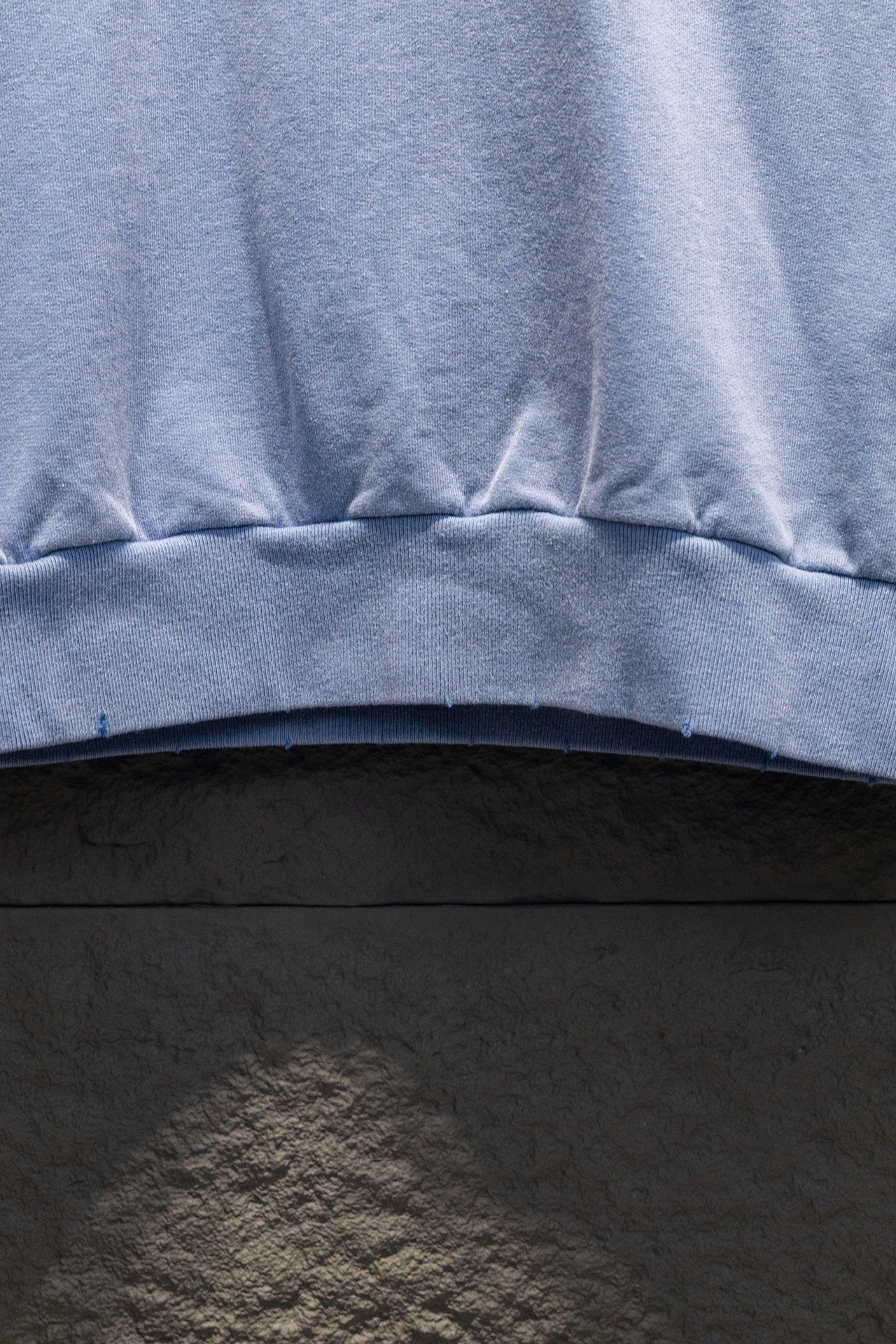 Light blue sweatshirt hem with ribbed band and stitched seam detail.