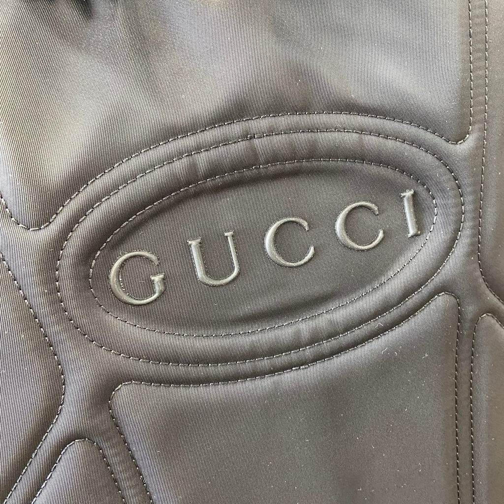 Close-up of Gucci logo patch on gray backpack with stitched oval emblem