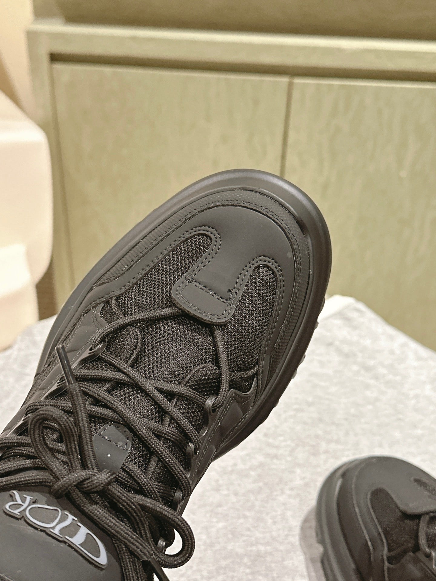 Dior unisex sneaker close-up, black upper with lace eyelets and mesh texture