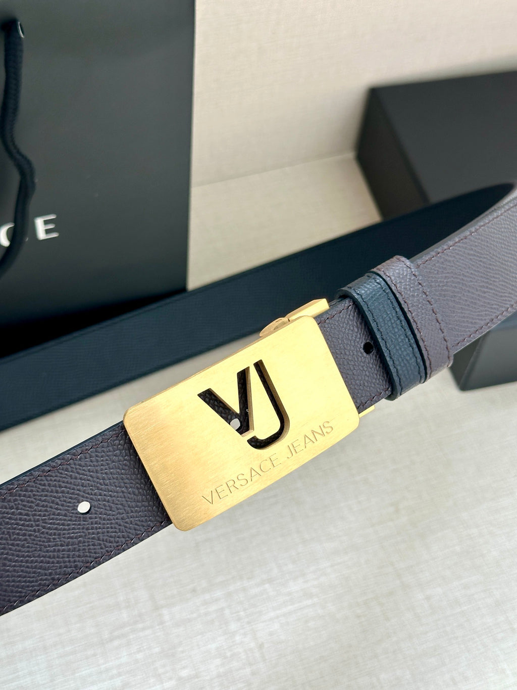 Leather belt with dark strap and gold buckle plate with VJ logo