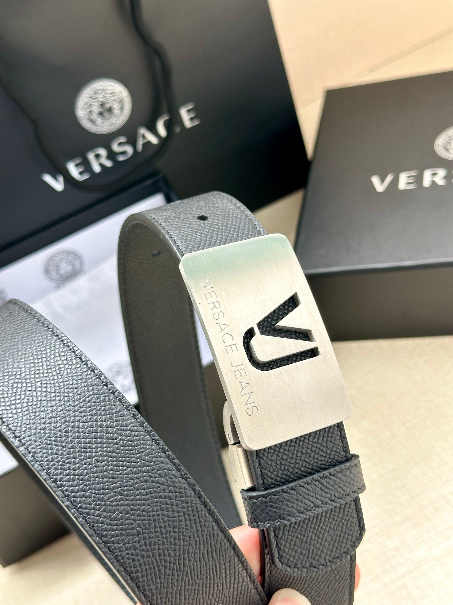 Close-up of dark blue leather belt with silver VJ logo buckle