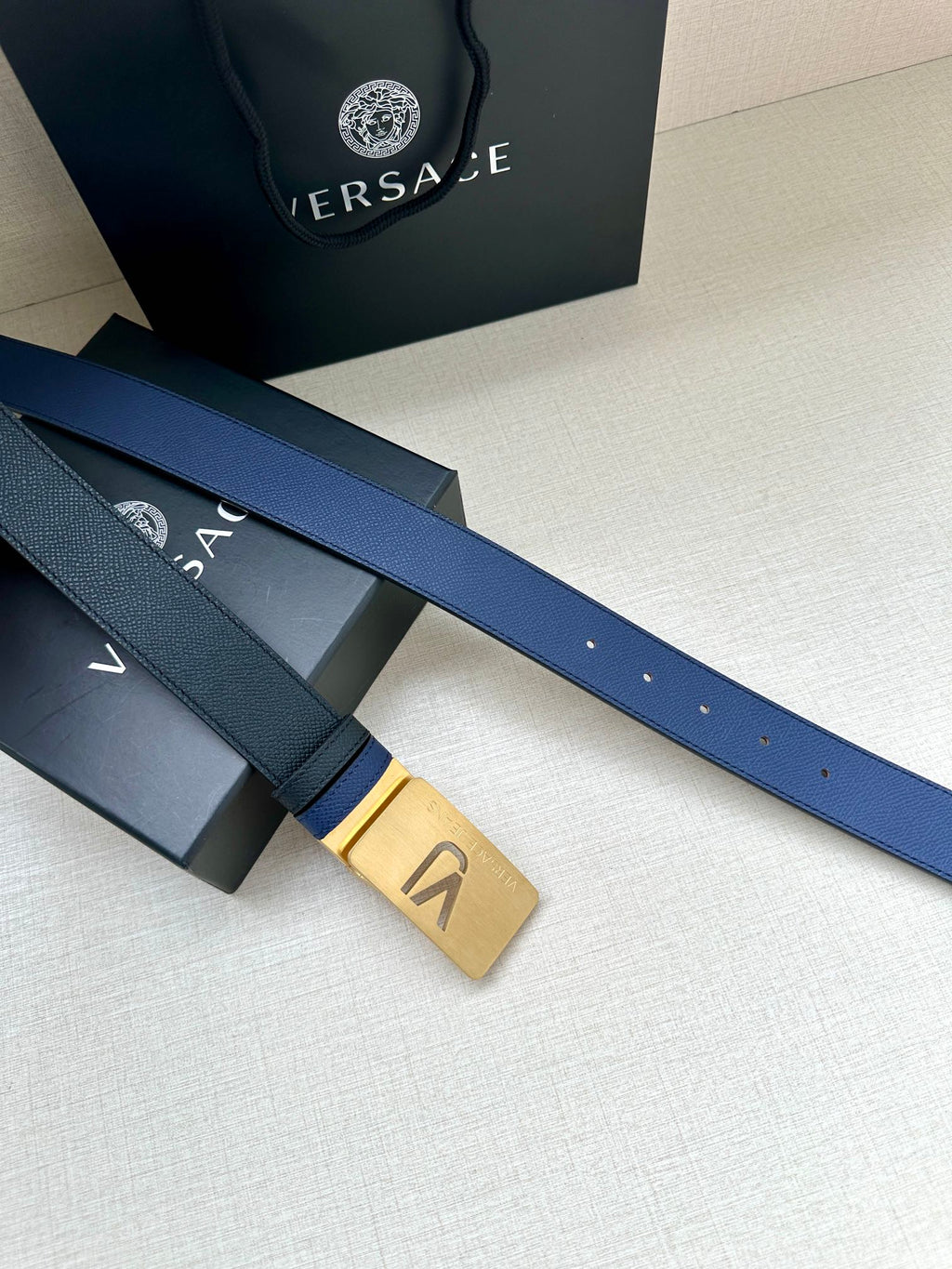 Versace blue leather belt with gold rectangular buckle and hole detail, close-up