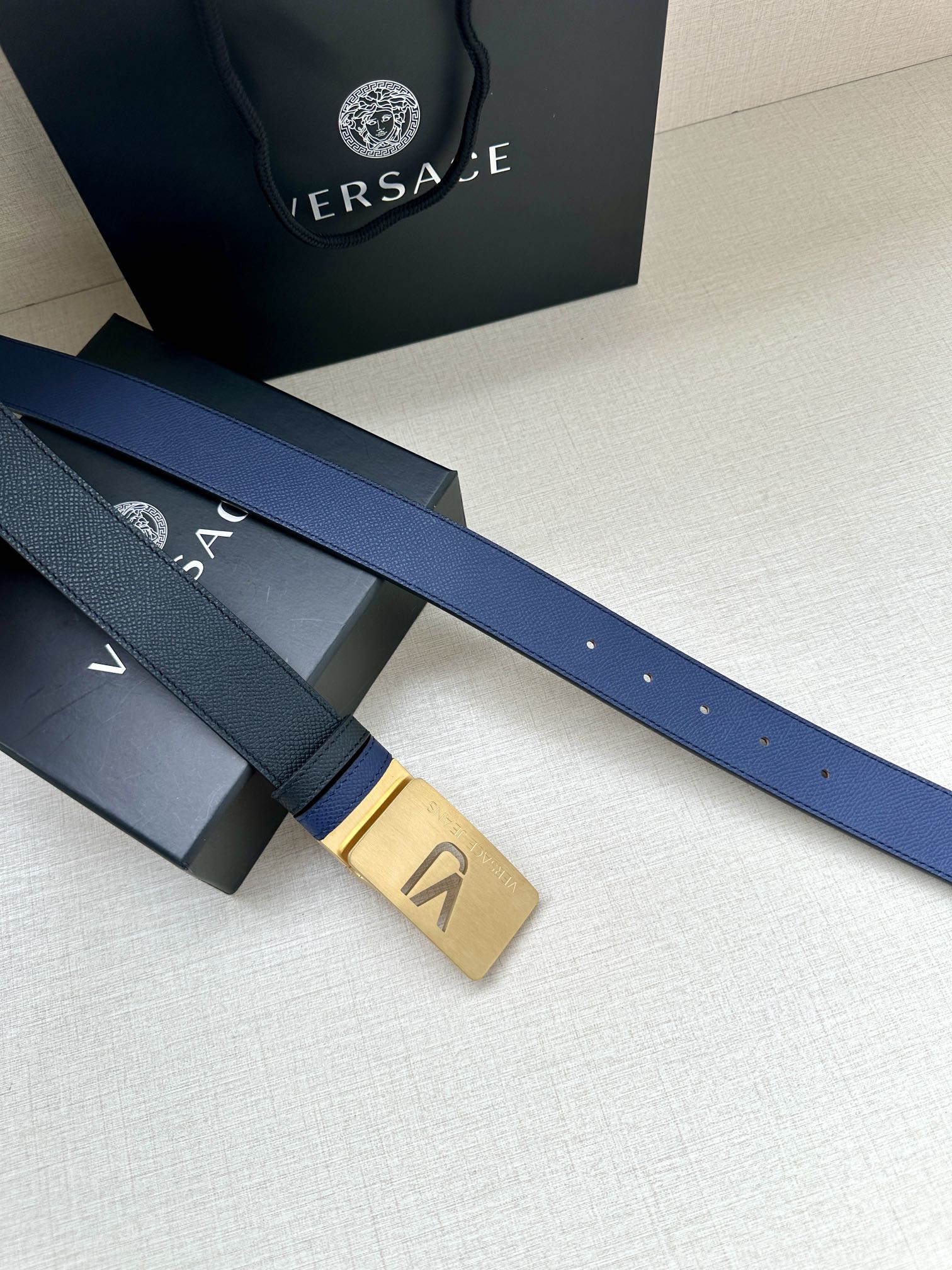 Versace blue leather belt with gold rectangular buckle and hole detail, close-up