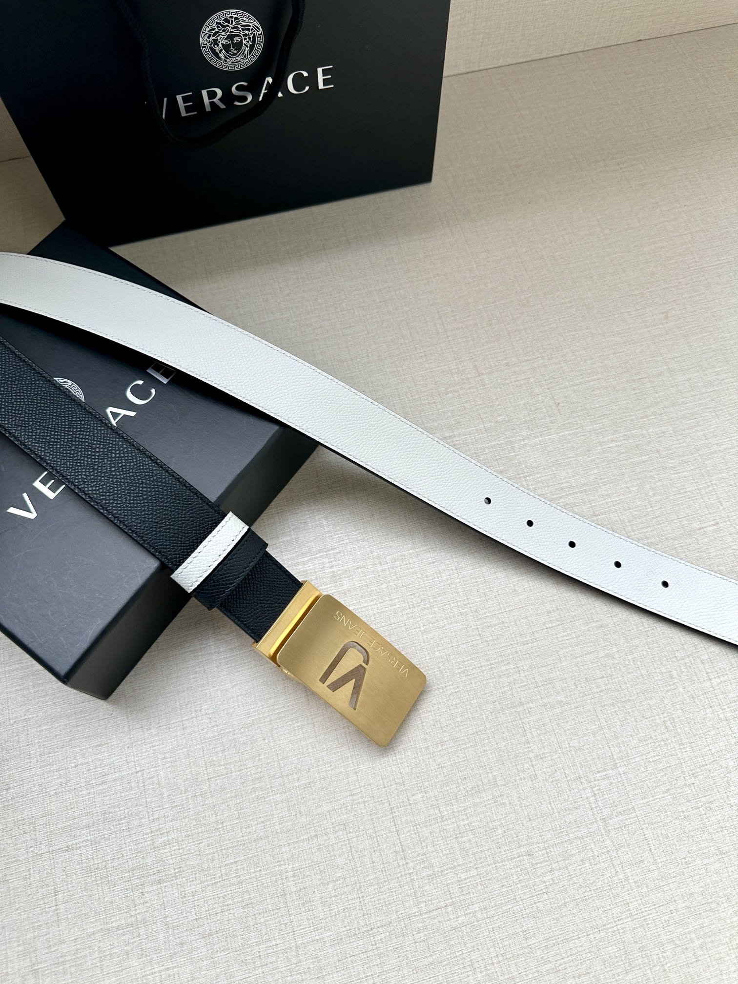 Versace belt showing gold square buckle and dark strap with white border stripe