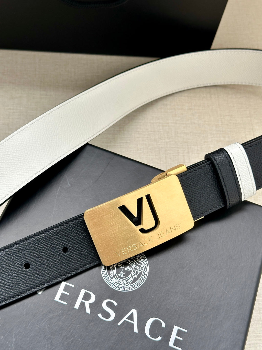 Versace belt with smooth dark leather, white stripes, and gold VJ logo buckle