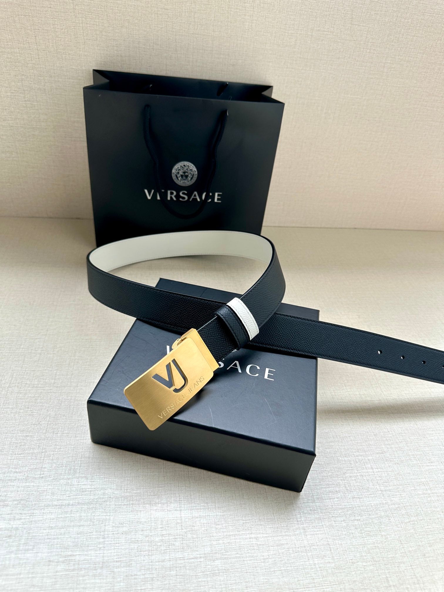 Versace belt with dark leather strap, white side stripes, and gold VJ buckle