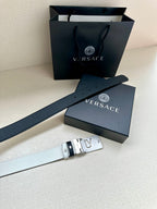 Versace belt with dark leather, white stripes, and gold buckle near gift box