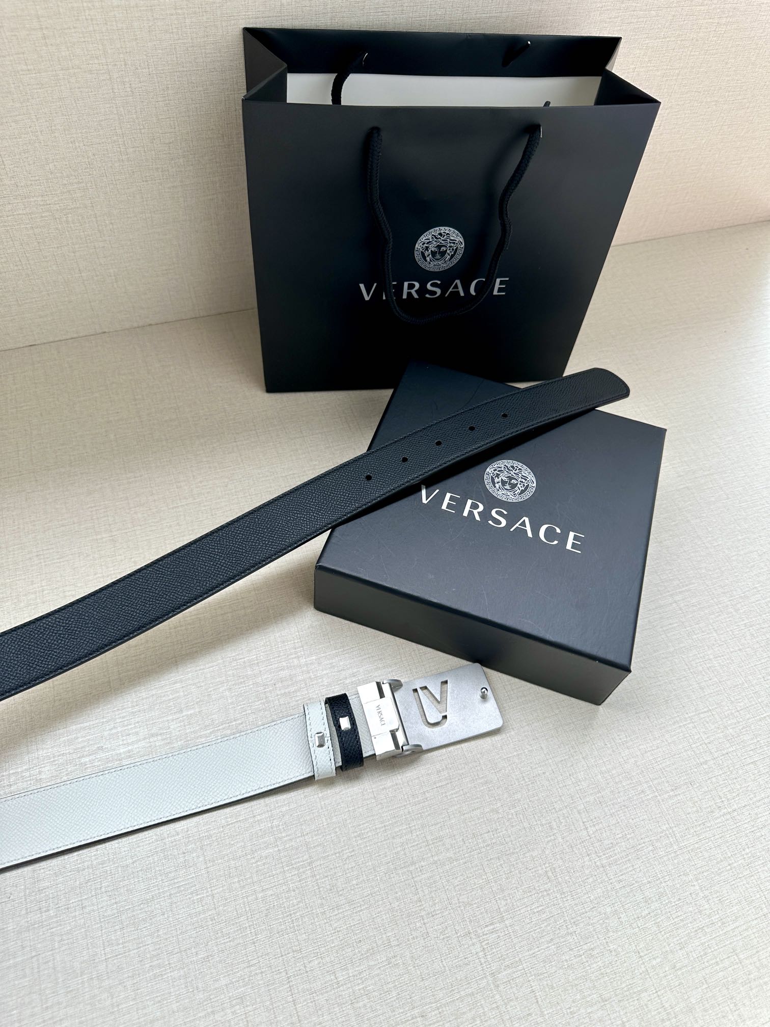 Versace belt with dark leather, white stripes, and gold buckle near gift box