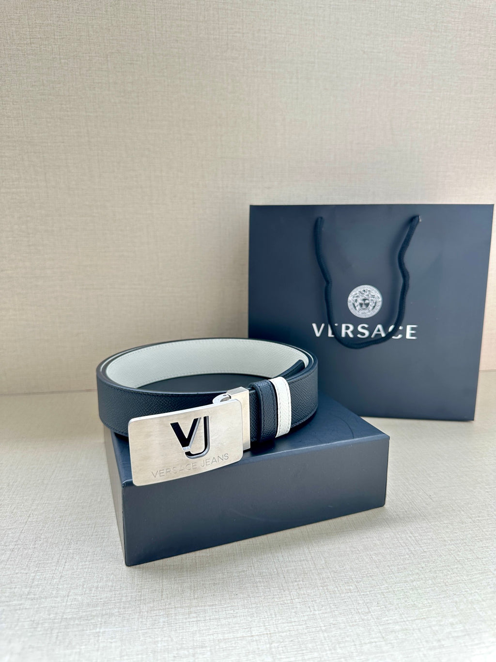 Versace belt laid on box: dark strap, white stripes, gold VJ logo buckle