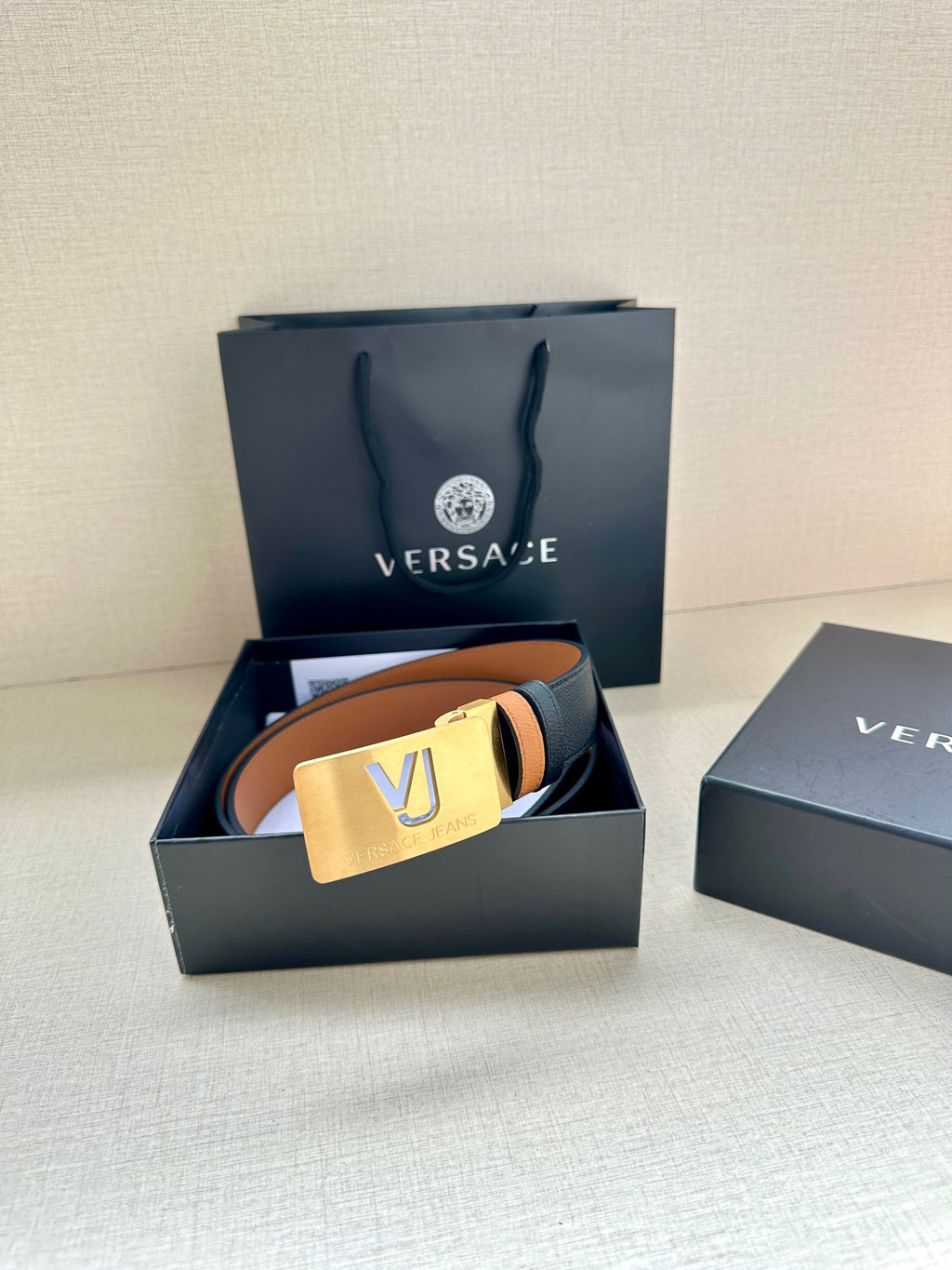 Versace belt with dark leather strap, tan underside, gold square VJ buckle.