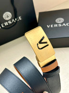 Versace belt buckle close-up: gold plate on dark leather with tan strap underside.