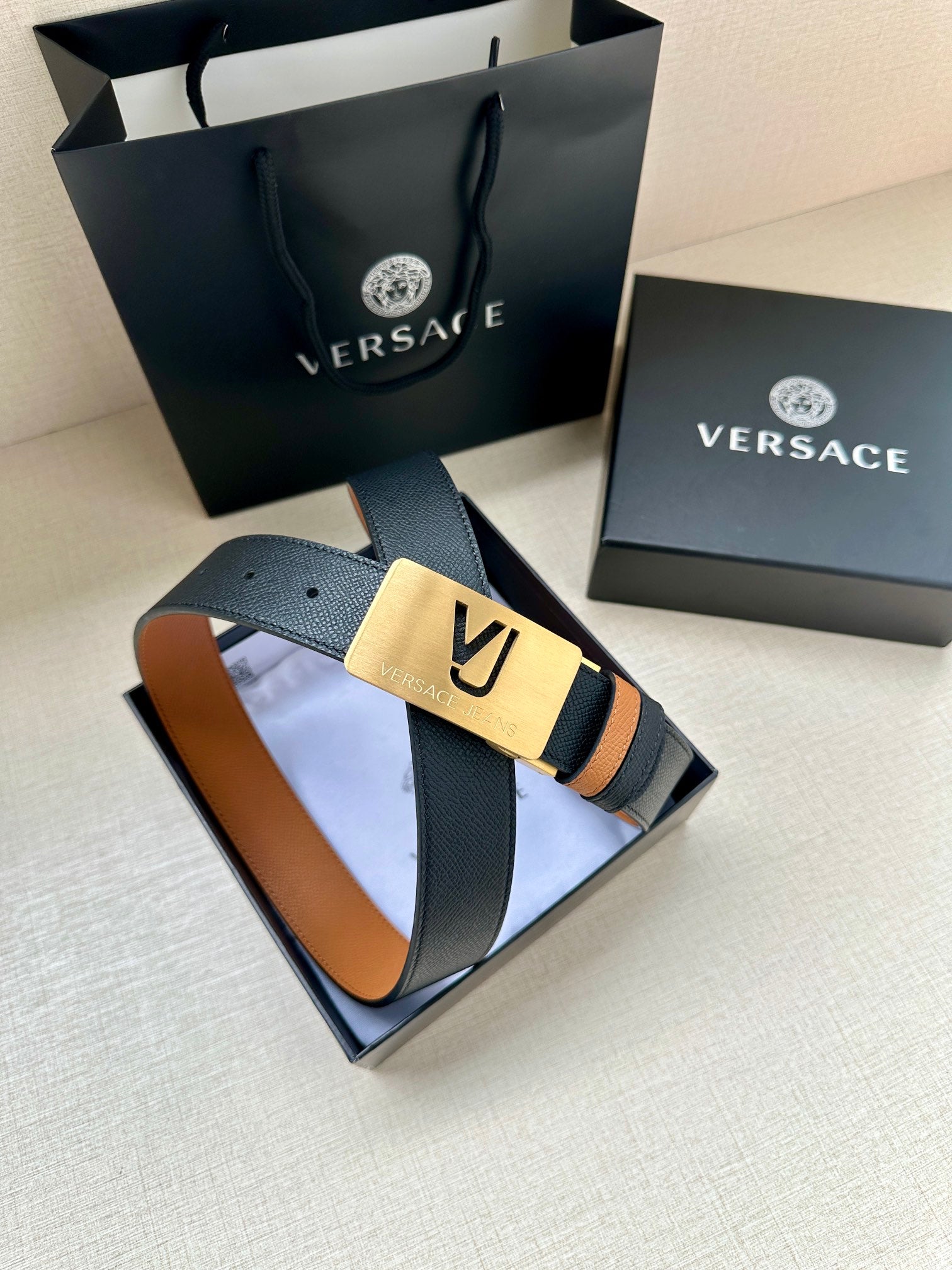 Versace belt in gift box: dark leather strap with tan underside and gold VJ buckle.