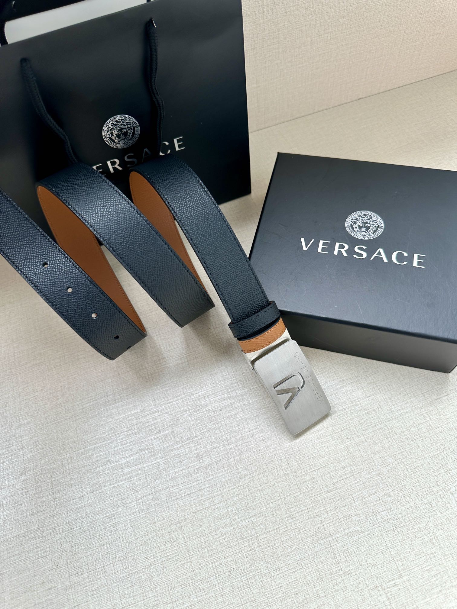 Versace belt with dark leather strap, tan underside, silver VJ buckle and holes.