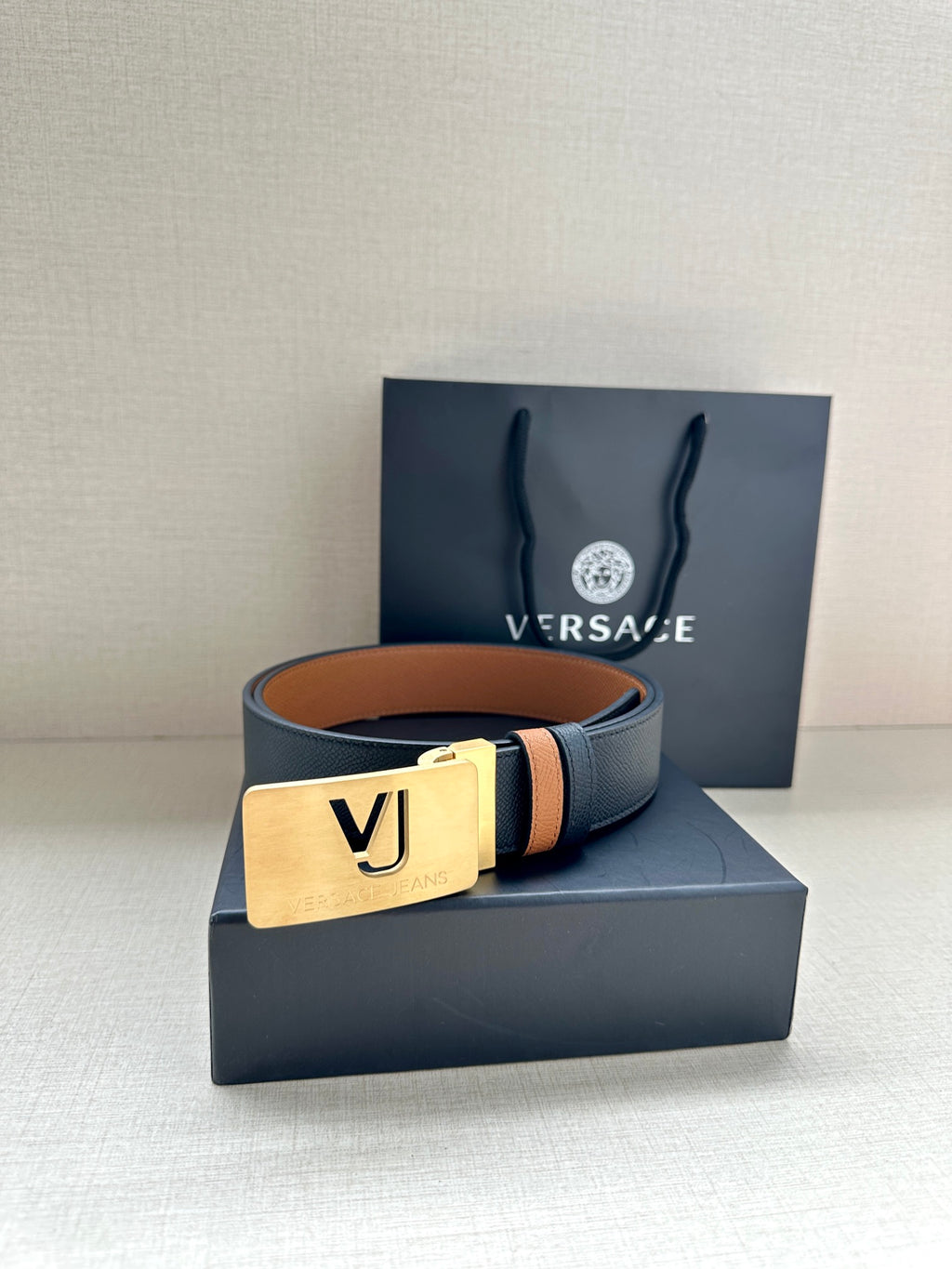 Versace belt with dark leather strap, tan underside, gold square VJ buckle.
