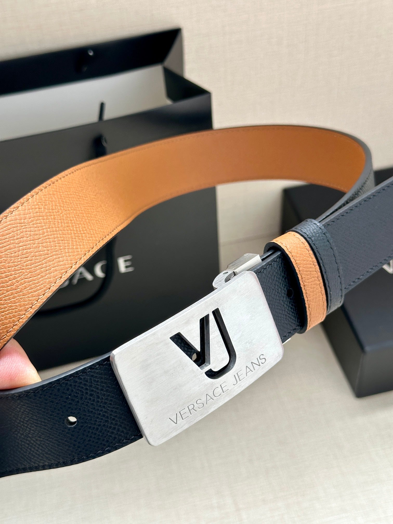 Versace belt detail: dark leather strap, tan underside, silver VJ buckle.