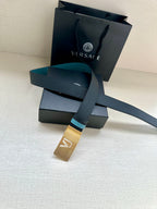 Dark leather belt with teal accents and gold buckle, laid over accessories boxes