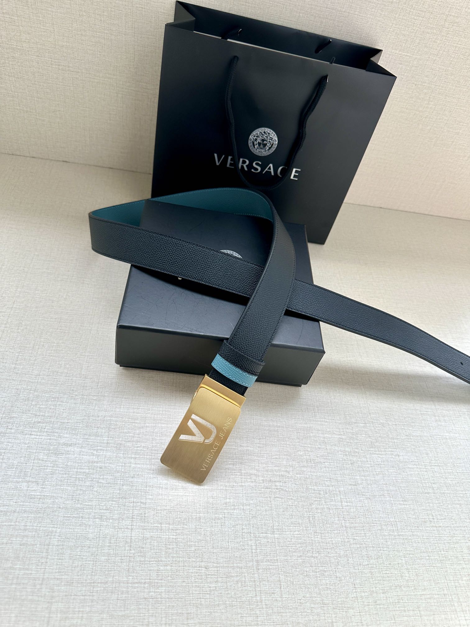 Dark leather belt with teal accents and gold buckle, laid over accessories boxes