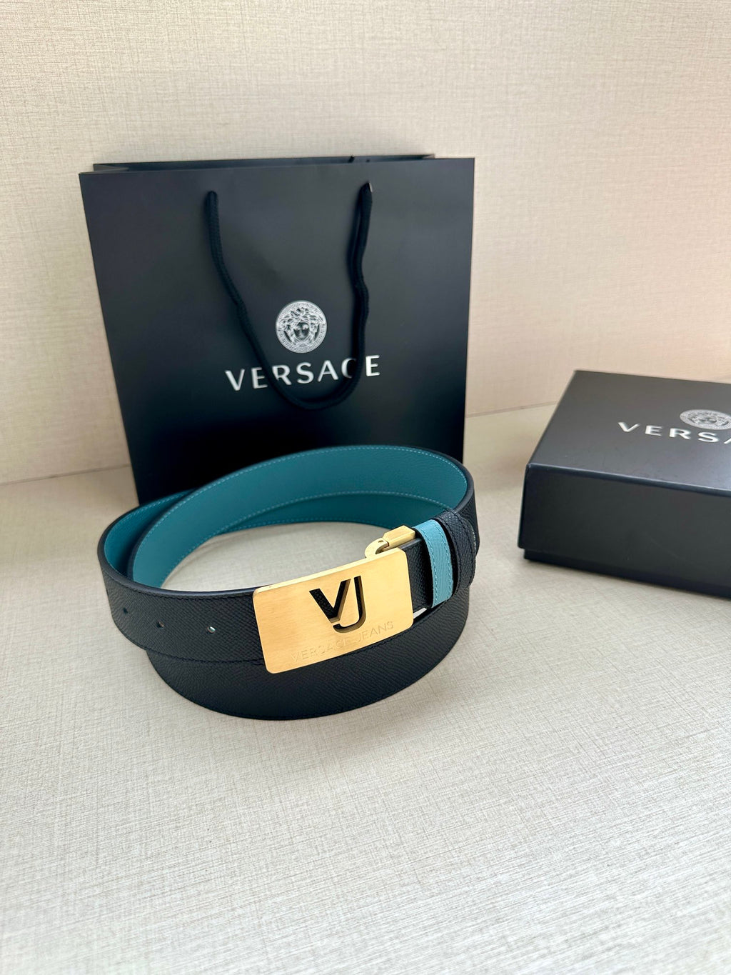 Teal and dark leather belt with gold VJ buckle on top of gift boxes