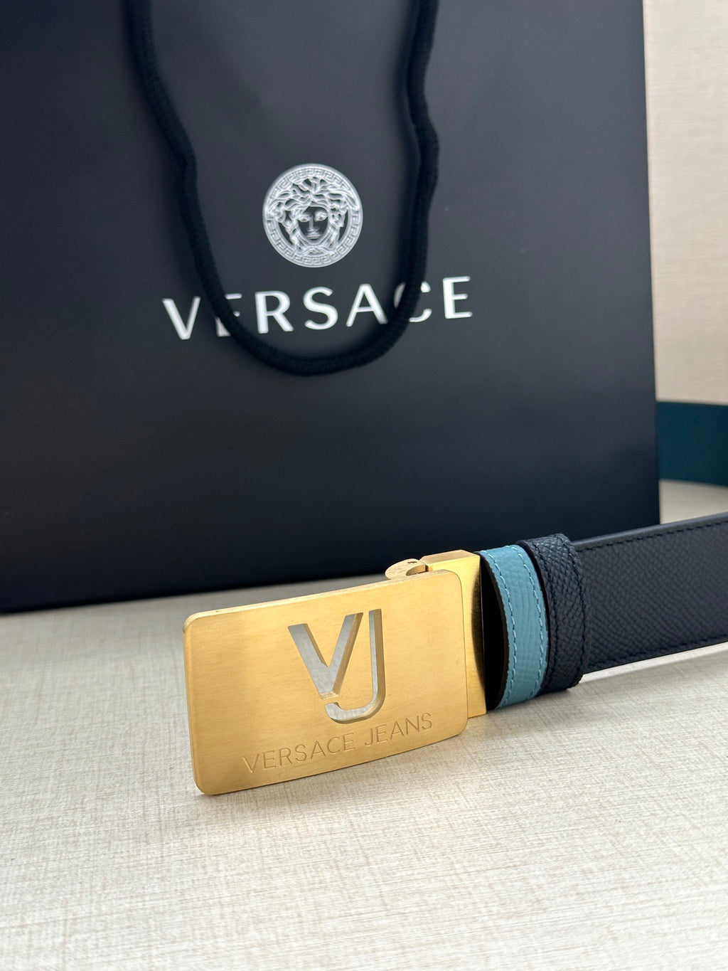 Gold VJ belt buckle on two-tone leather strap, with logo branding on packaging