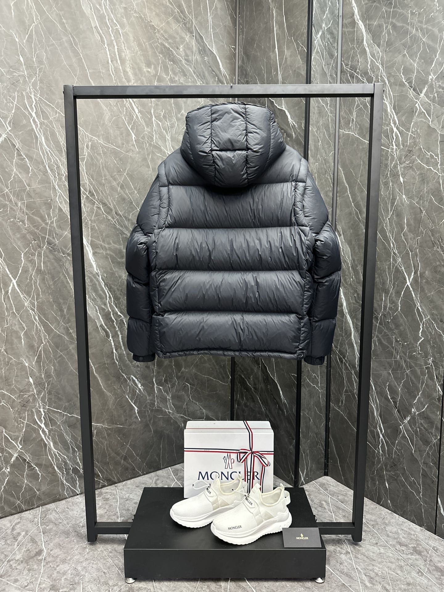 Long back view of hooded puffer jacket, dark quilted fabric and ribbed cuffs