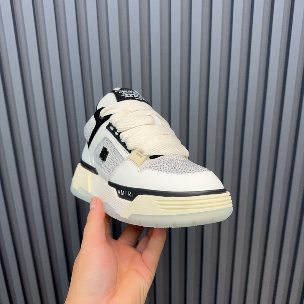 White low-top sneakers with black accents, cream sole, lace-up and logo patch.