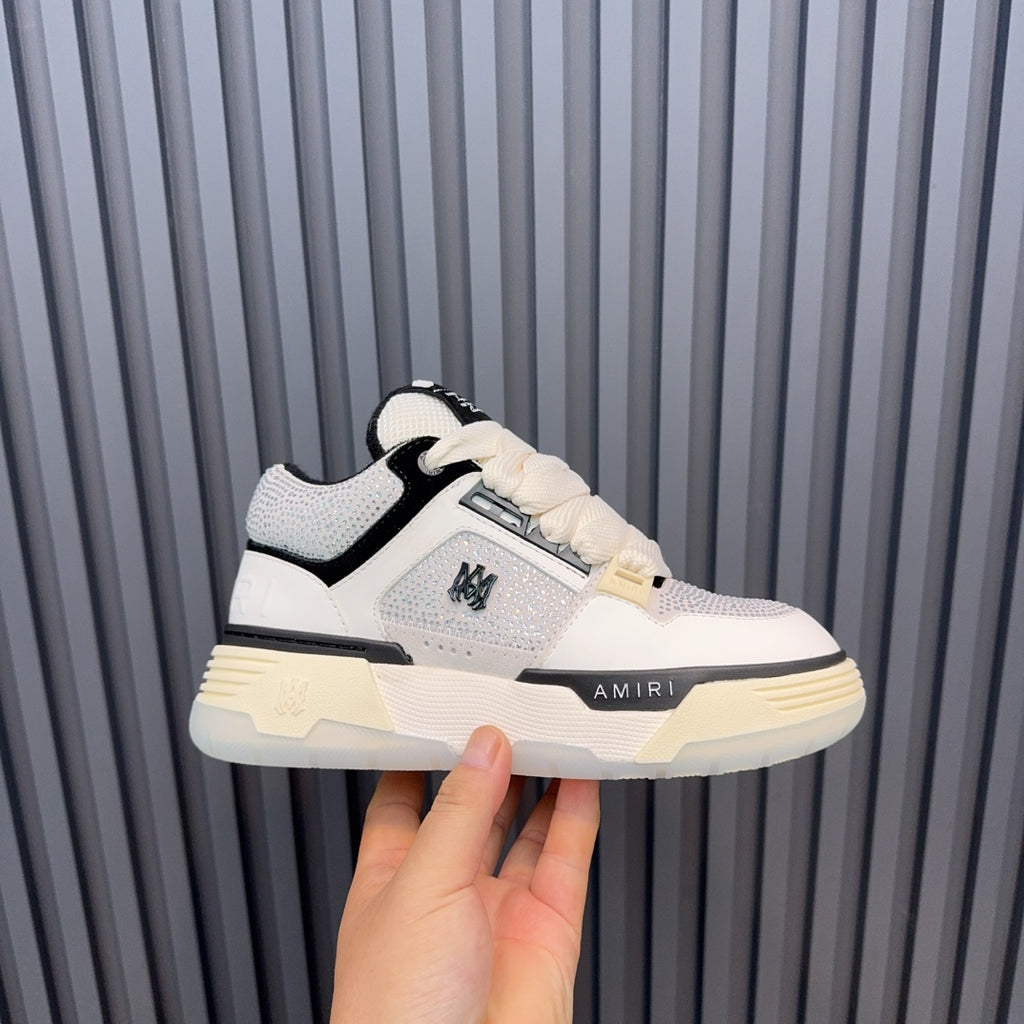 White and black low-top sneakers with cream sole and AMIRI side logo.