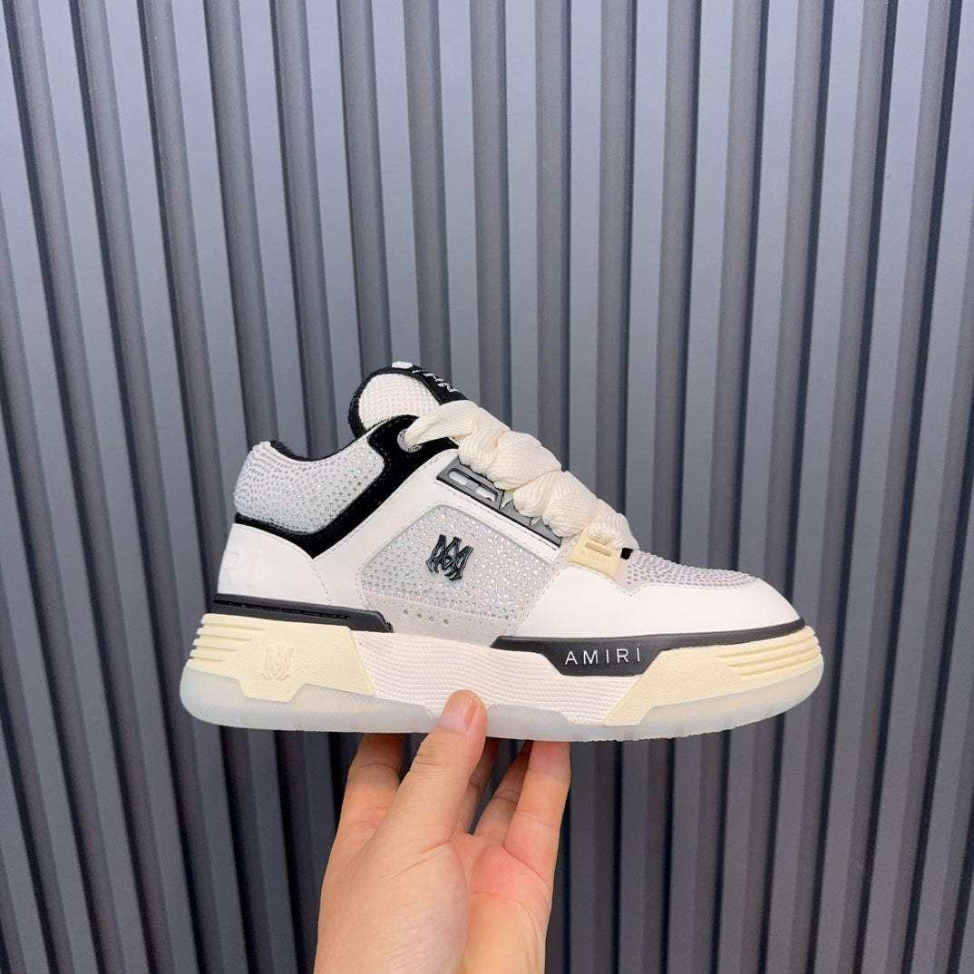 White and black low-top sneakers with cream sole and AMIRI side logo.