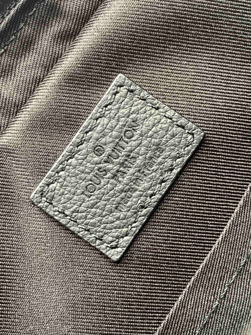 Louis Vuitton bag interior label on textured gray fabric with embossed logo