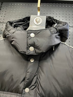 Black hooded puffer jacket with snap buttons and large round logo patch